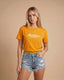 Woman wearing an orange t-shirt with 'Montavor' text and denim shorts on a beige background