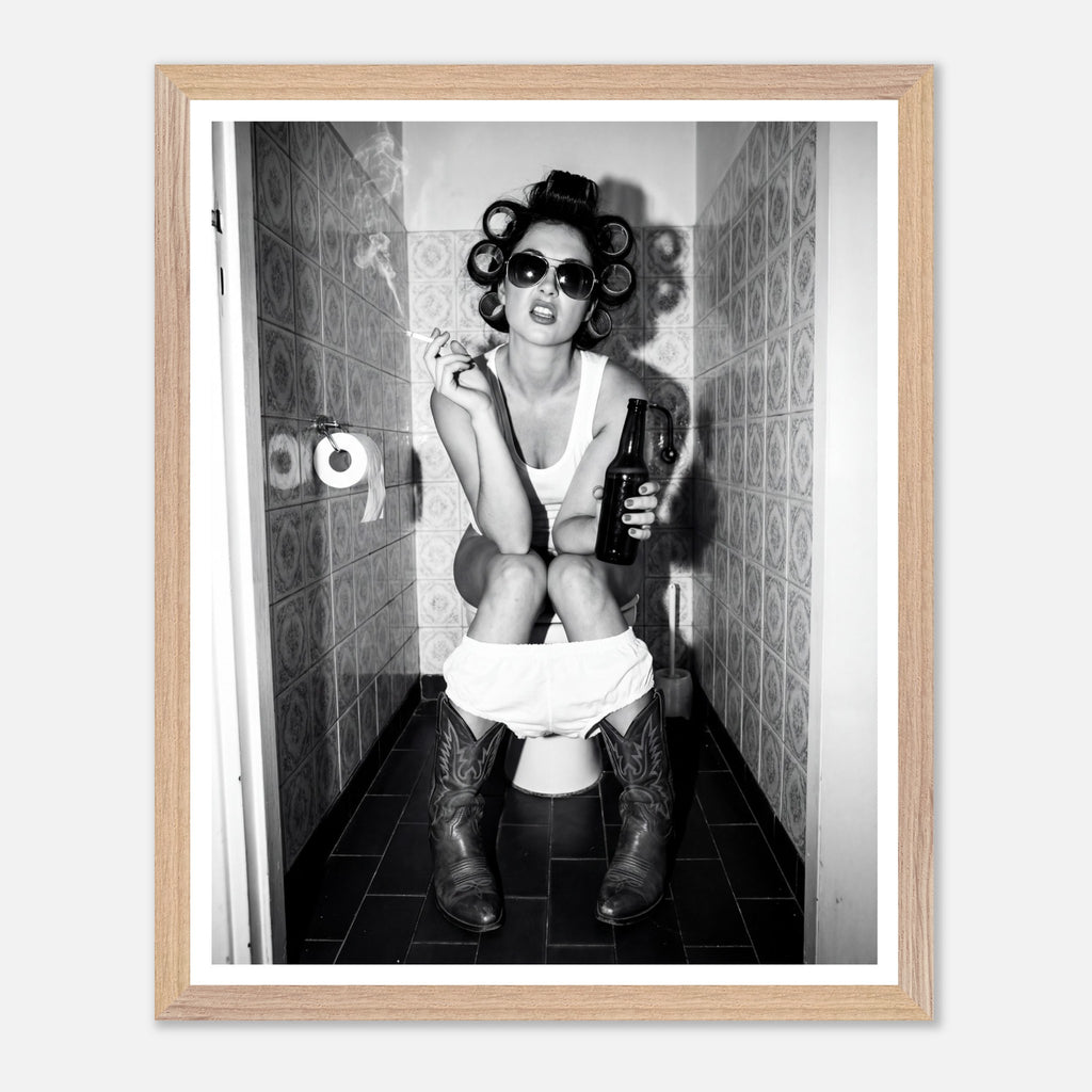 Black and white photograph of a rebellious cowgirl wearing cowboy boots and sunglasses sitting in a tiled restroom holding a cigarette and beer.