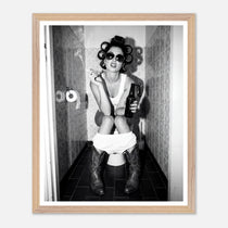 Black and white photograph of a rebellious cowgirl wearing cowboy boots and sunglasses sitting in a tiled restroom holding a cigarette and beer.