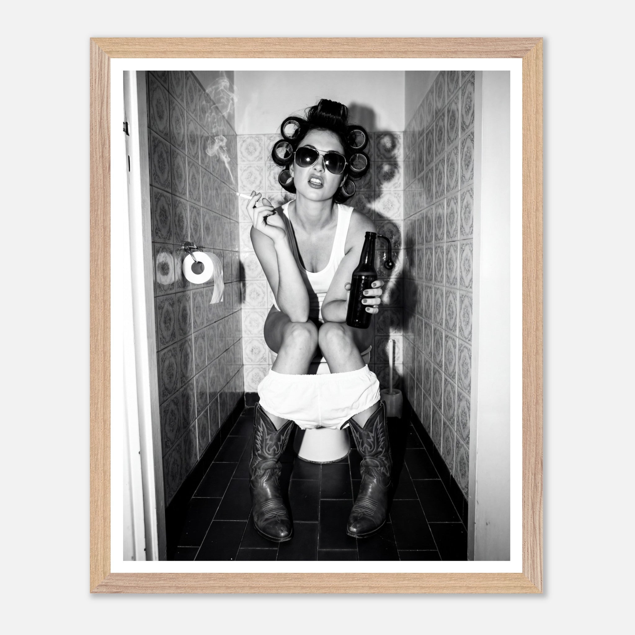 Black and white photograph of a rebellious cowgirl wearing cowboy boots and sunglasses sitting in a tiled restroom holding a cigarette and beer.