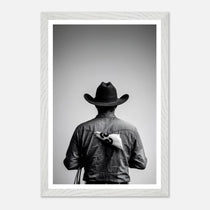 Black and white photograph of a rodeo cowboy viewed from behind wearing a western hat with a numbered rodeo tag pinned to his shirt after competition.