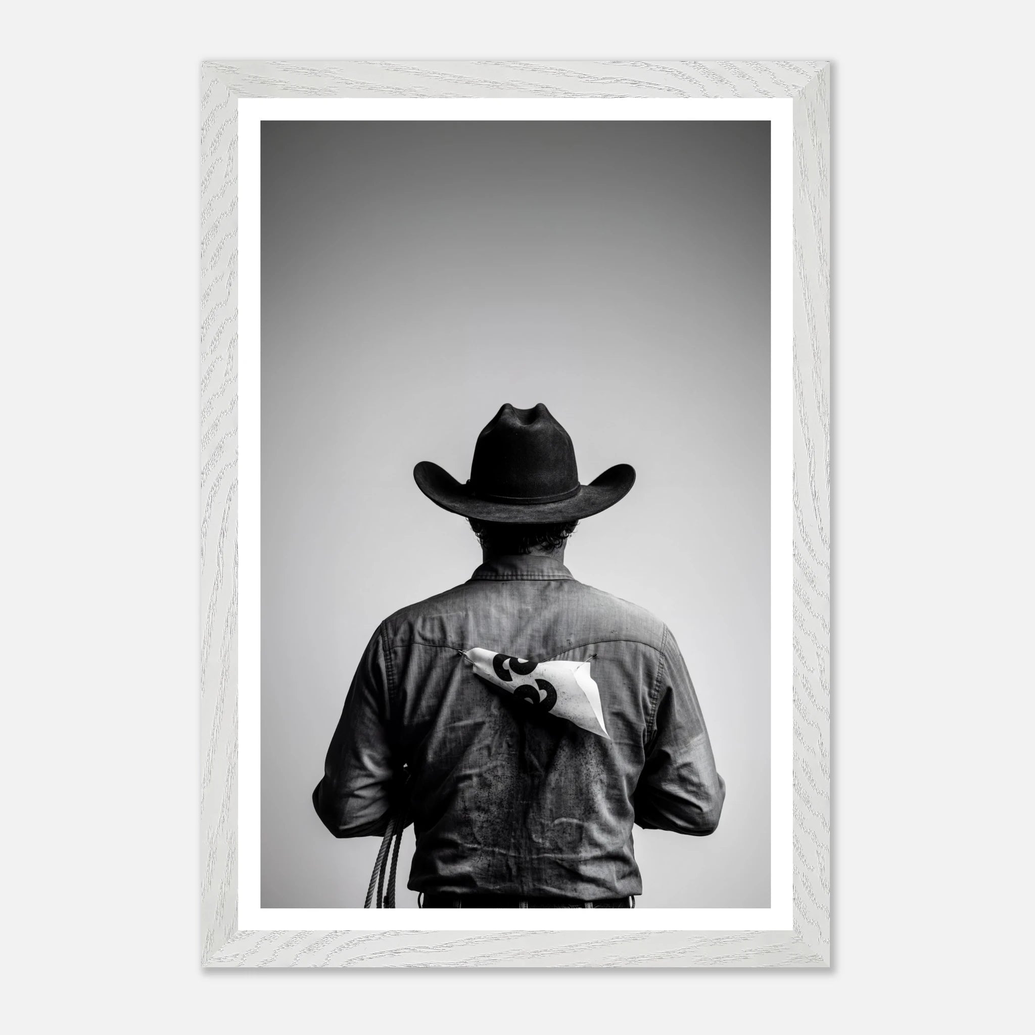 Black and white photograph of a rodeo cowboy viewed from behind wearing a western hat with a numbered rodeo tag pinned to his shirt after competition.