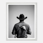Black and white photograph of a rodeo cowboy viewed from behind wearing a western hat with a numbered rodeo tag pinned to his shirt after competition.