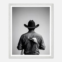 Black and white photograph of a rodeo cowboy viewed from behind wearing a western hat with a numbered rodeo tag pinned to his shirt after competition.
