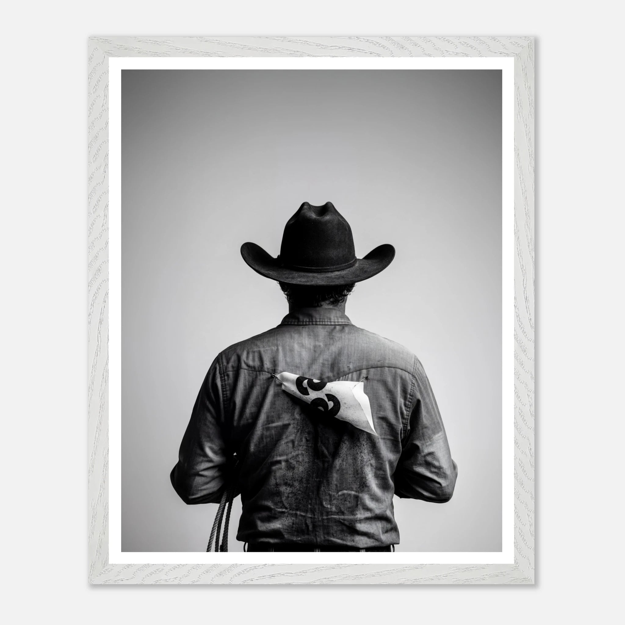 Black and white photograph of a rodeo cowboy viewed from behind wearing a western hat with a numbered rodeo tag pinned to his shirt after competition.