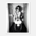 Black and white photograph of a rebellious cowgirl wearing cowboy boots and sunglasses sitting in a tiled restroom holding a cigarette and beer.