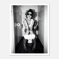 Black and white photograph of a rebellious cowgirl wearing cowboy boots and sunglasses sitting in a tiled restroom holding a cigarette and beer.