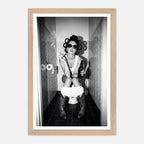 Black and white photograph of a rebellious cowgirl wearing cowboy boots and sunglasses sitting in a tiled restroom holding a cigarette and beer.