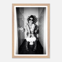 Black and white photograph of a rebellious cowgirl wearing cowboy boots and sunglasses sitting in a tiled restroom holding a cigarette and beer.