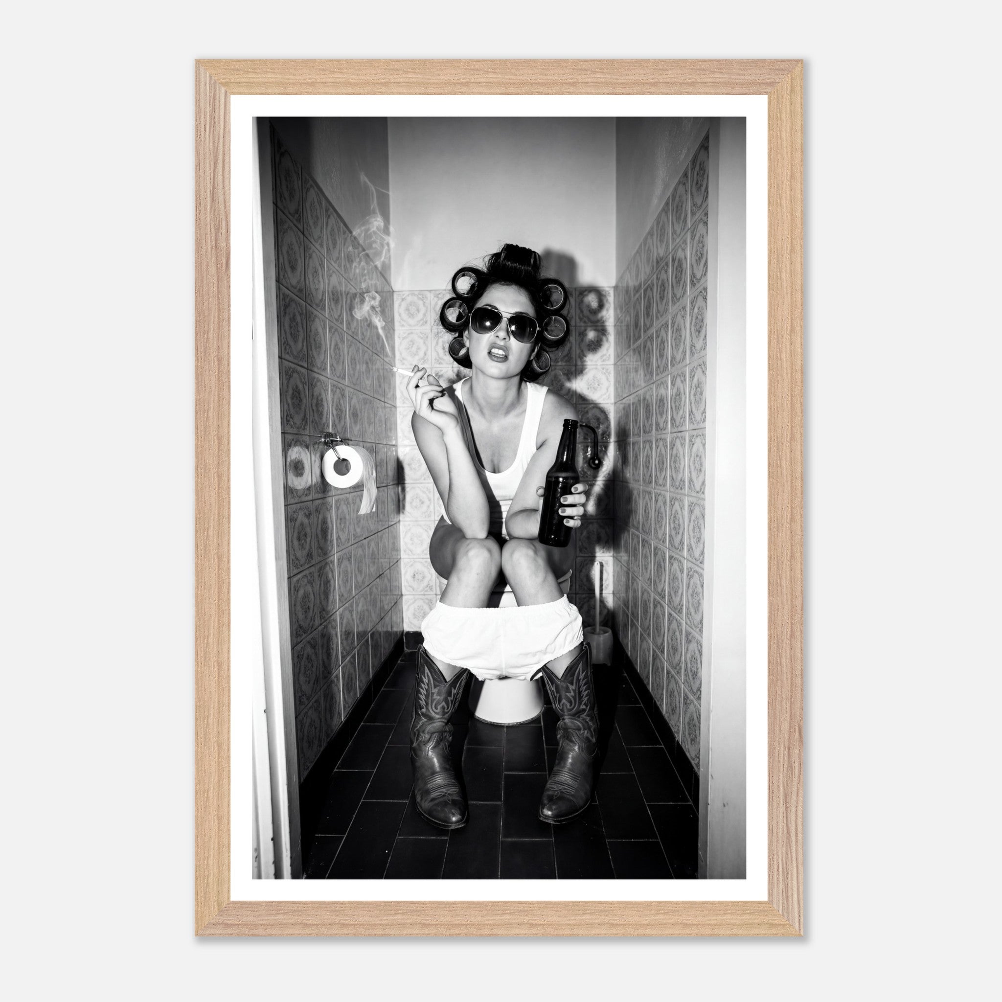 Black and white photograph of a rebellious cowgirl wearing cowboy boots and sunglasses sitting in a tiled restroom holding a cigarette and beer.