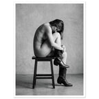 Black and white fine art photograph of a woman seated on a stool wearing cowboy boots in a minimalist studio setting.