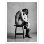Black and white fine art photograph of a woman seated on a stool wearing cowboy boots in a minimalist studio setting.