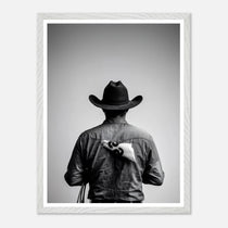 Black and white photograph of a rodeo cowboy viewed from behind wearing a western hat with a numbered rodeo tag pinned to his shirt after competition.