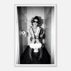 Black and white photograph of a rebellious cowgirl wearing cowboy boots and sunglasses sitting in a tiled restroom holding a cigarette and beer.