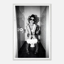 Black and white photograph of a rebellious cowgirl wearing cowboy boots and sunglasses sitting in a tiled restroom holding a cigarette and beer.