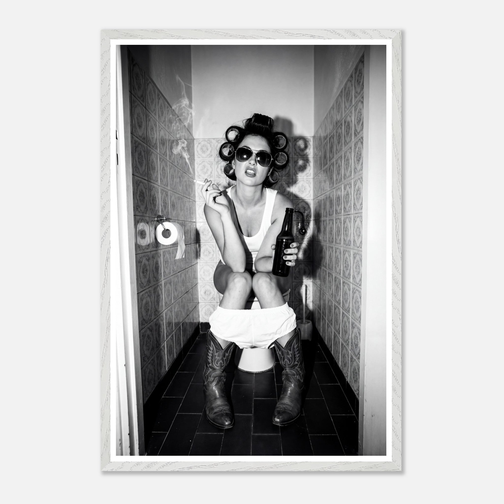 Black and white photograph of a rebellious cowgirl wearing cowboy boots and sunglasses sitting in a tiled restroom holding a cigarette and beer.