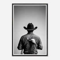 Black and white photograph of a rodeo cowboy viewed from behind wearing a western hat with a numbered rodeo tag pinned to his shirt after competition.