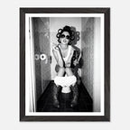 Black and white photograph of a rebellious cowgirl wearing cowboy boots and sunglasses sitting in a tiled restroom holding a cigarette and beer.