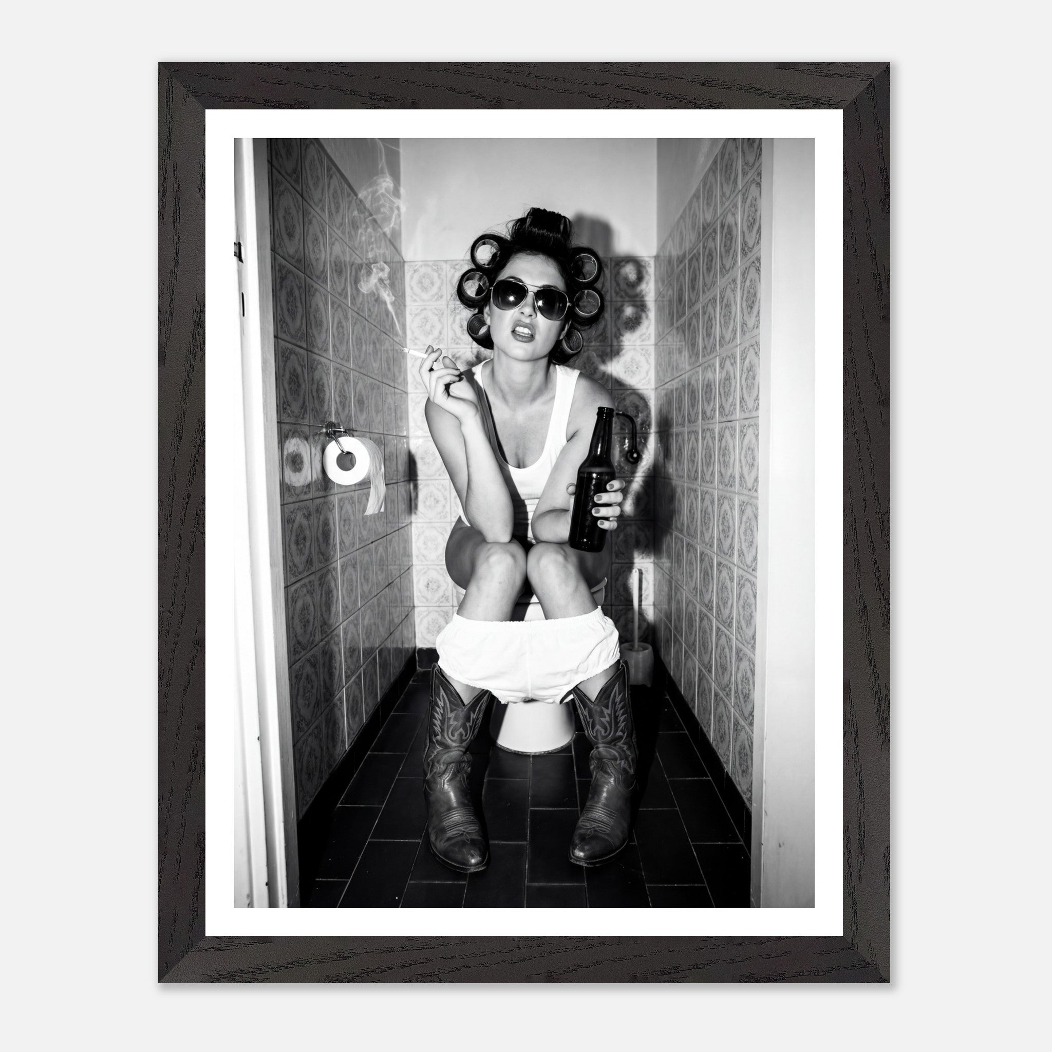 Black and white photograph of a rebellious cowgirl wearing cowboy boots and sunglasses sitting in a tiled restroom holding a cigarette and beer.