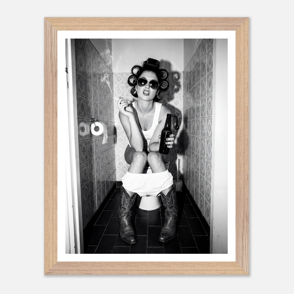 Black and white photograph of a rebellious cowgirl wearing cowboy boots and sunglasses sitting in a tiled restroom holding a cigarette and beer.