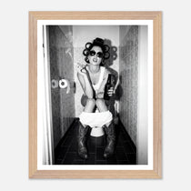 Black and white photograph of a rebellious cowgirl wearing cowboy boots and sunglasses sitting in a tiled restroom holding a cigarette and beer.