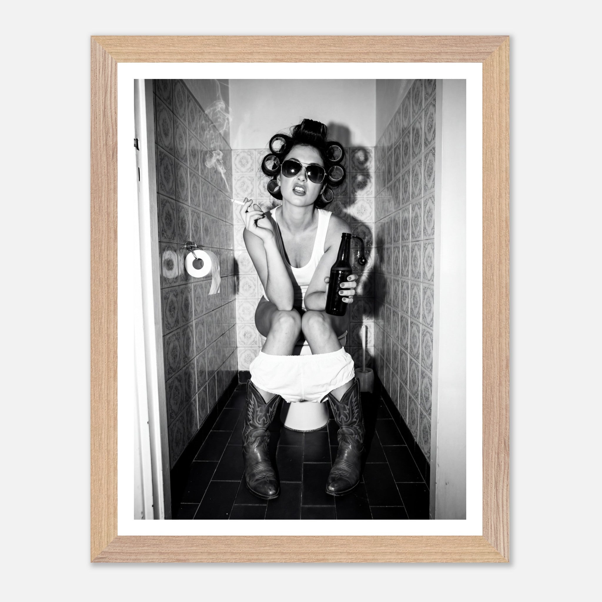 Black and white photograph of a rebellious cowgirl wearing cowboy boots and sunglasses sitting in a tiled restroom holding a cigarette and beer.