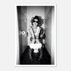 Black and white photograph of a rebellious cowgirl wearing cowboy boots and sunglasses sitting in a tiled restroom holding a cigarette and beer.