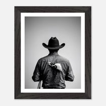 Black and white photograph of a rodeo cowboy viewed from behind wearing a western hat with a numbered rodeo tag pinned to his shirt after competition.