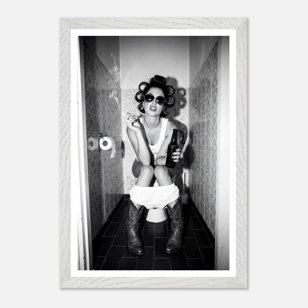 Black and white photograph of a rebellious cowgirl wearing cowboy boots and sunglasses sitting in a tiled restroom holding a cigarette and beer.