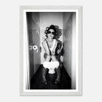 Black and white photograph of a rebellious cowgirl wearing cowboy boots and sunglasses sitting in a tiled restroom holding a cigarette and beer.
