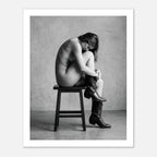 Black and white fine art photograph of a woman seated on a stool wearing cowboy boots in a minimalist studio setting.