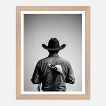 Black and white photograph of a rodeo cowboy viewed from behind wearing a western hat with a numbered rodeo tag pinned to his shirt after competition.