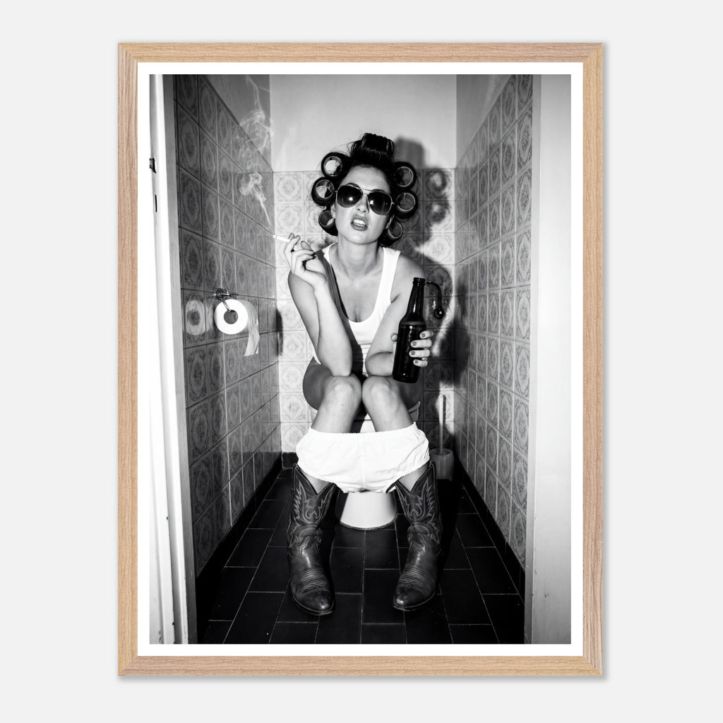 Black and white photograph of a rebellious cowgirl wearing cowboy boots and sunglasses sitting in a tiled restroom holding a cigarette and beer.