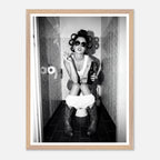 Black and white photograph of a rebellious cowgirl wearing cowboy boots and sunglasses sitting in a tiled restroom holding a cigarette and beer.