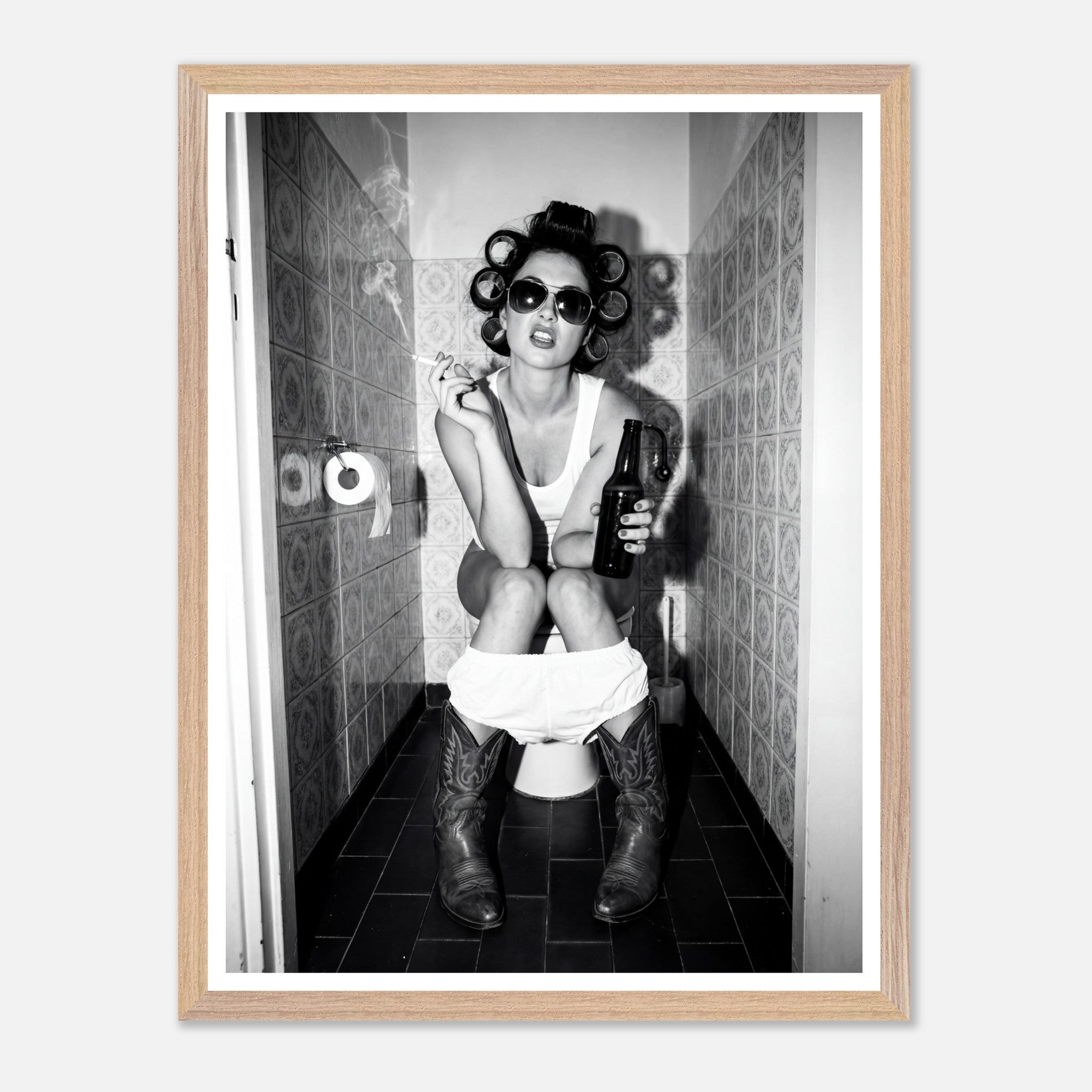 Black and white photograph of a rebellious cowgirl wearing cowboy boots and sunglasses sitting in a tiled restroom holding a cigarette and beer.