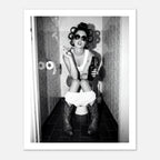 Black and white photograph of a rebellious cowgirl wearing cowboy boots and sunglasses sitting in a tiled restroom holding a cigarette and beer.