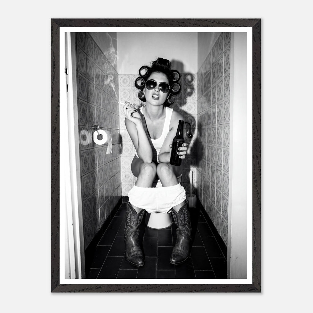 Black and white photograph of a rebellious cowgirl wearing cowboy boots and sunglasses sitting in a tiled restroom holding a cigarette and beer.