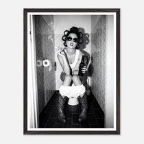 Black and white photograph of a rebellious cowgirl wearing cowboy boots and sunglasses sitting in a tiled restroom holding a cigarette and beer.