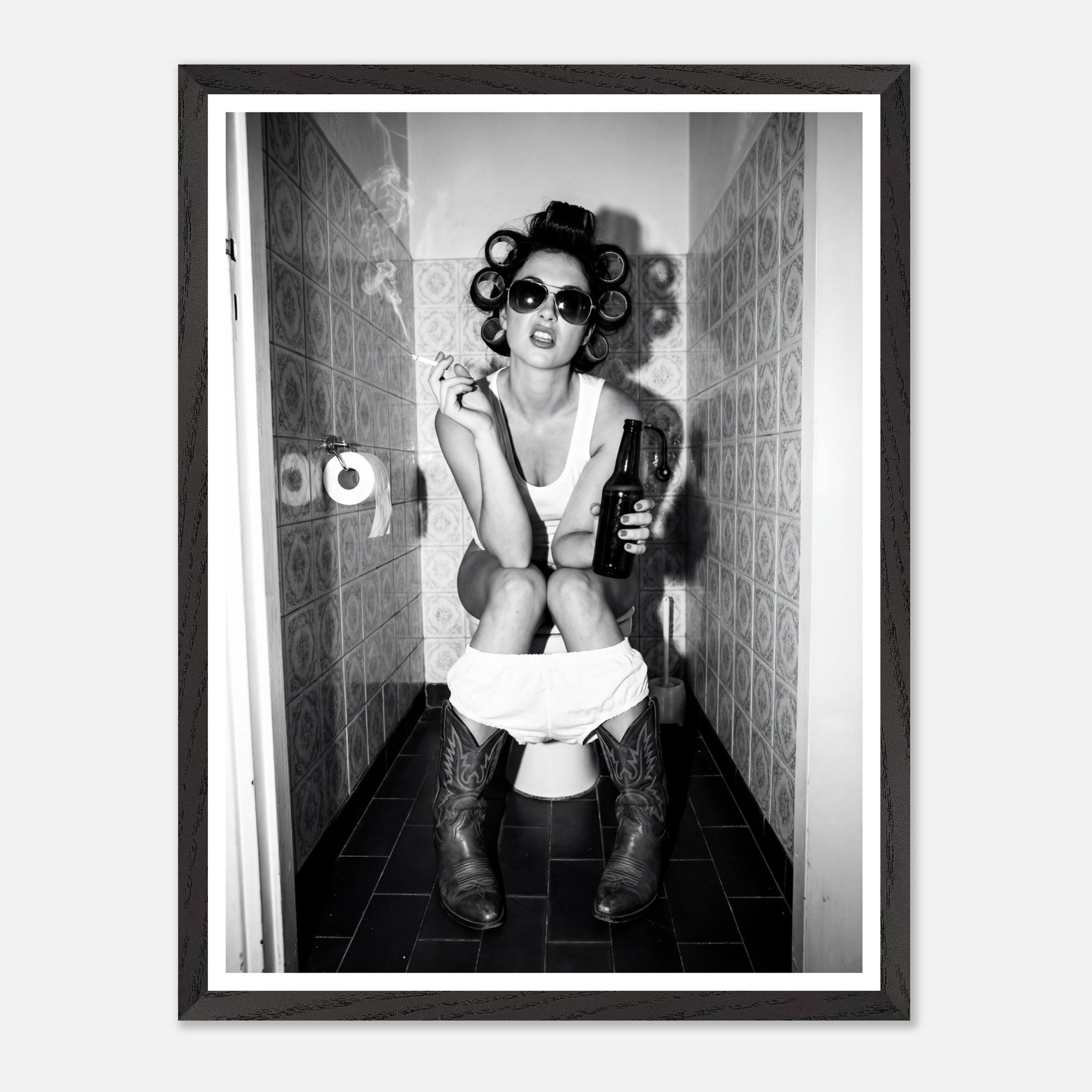 Black and white photograph of a rebellious cowgirl wearing cowboy boots and sunglasses sitting in a tiled restroom holding a cigarette and beer.