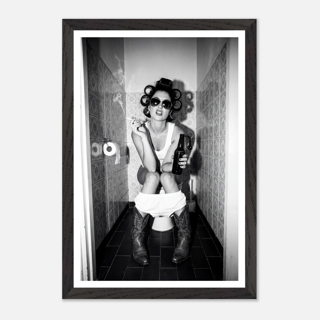 Black and white photograph of a rebellious cowgirl wearing cowboy boots and sunglasses sitting in a tiled restroom holding a cigarette and beer.