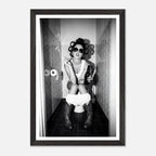 Black and white photograph of a rebellious cowgirl wearing cowboy boots and sunglasses sitting in a tiled restroom holding a cigarette and beer.