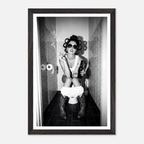 Black and white photograph of a rebellious cowgirl wearing cowboy boots and sunglasses sitting in a tiled restroom holding a cigarette and beer.