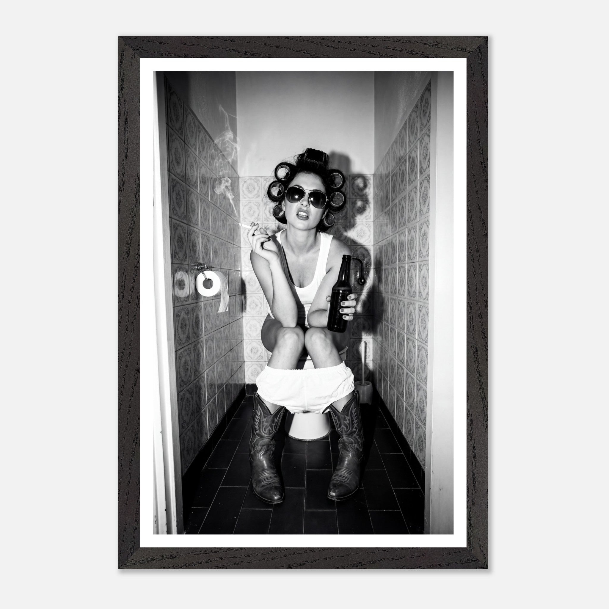 Black and white photograph of a rebellious cowgirl wearing cowboy boots and sunglasses sitting in a tiled restroom holding a cigarette and beer.