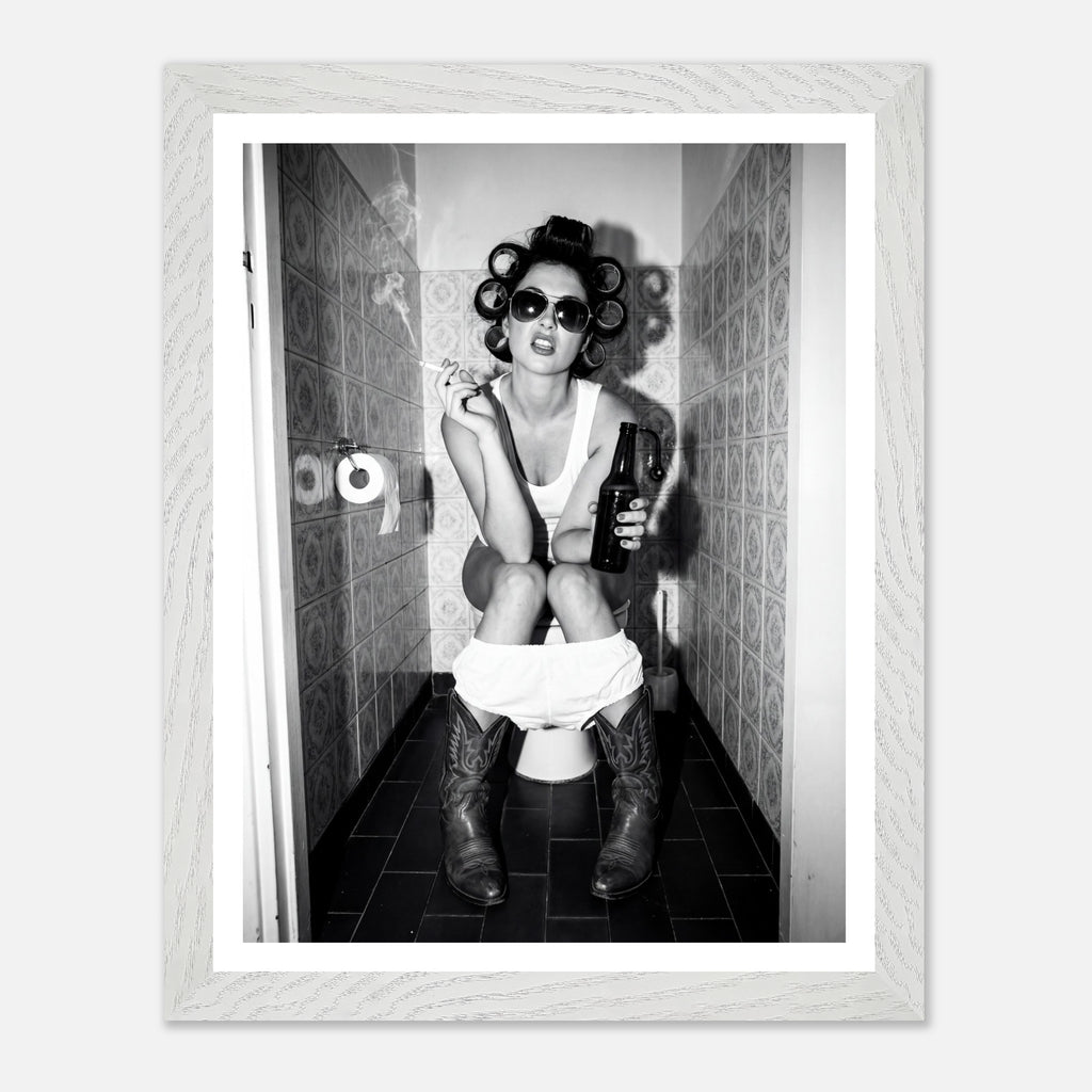 Black and white photograph of a rebellious cowgirl wearing cowboy boots and sunglasses sitting in a tiled restroom holding a cigarette and beer.