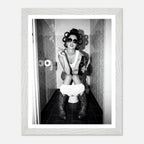 Black and white photograph of a rebellious cowgirl wearing cowboy boots and sunglasses sitting in a tiled restroom holding a cigarette and beer.
