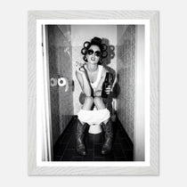 Black and white photograph of a rebellious cowgirl wearing cowboy boots and sunglasses sitting in a tiled restroom holding a cigarette and beer.