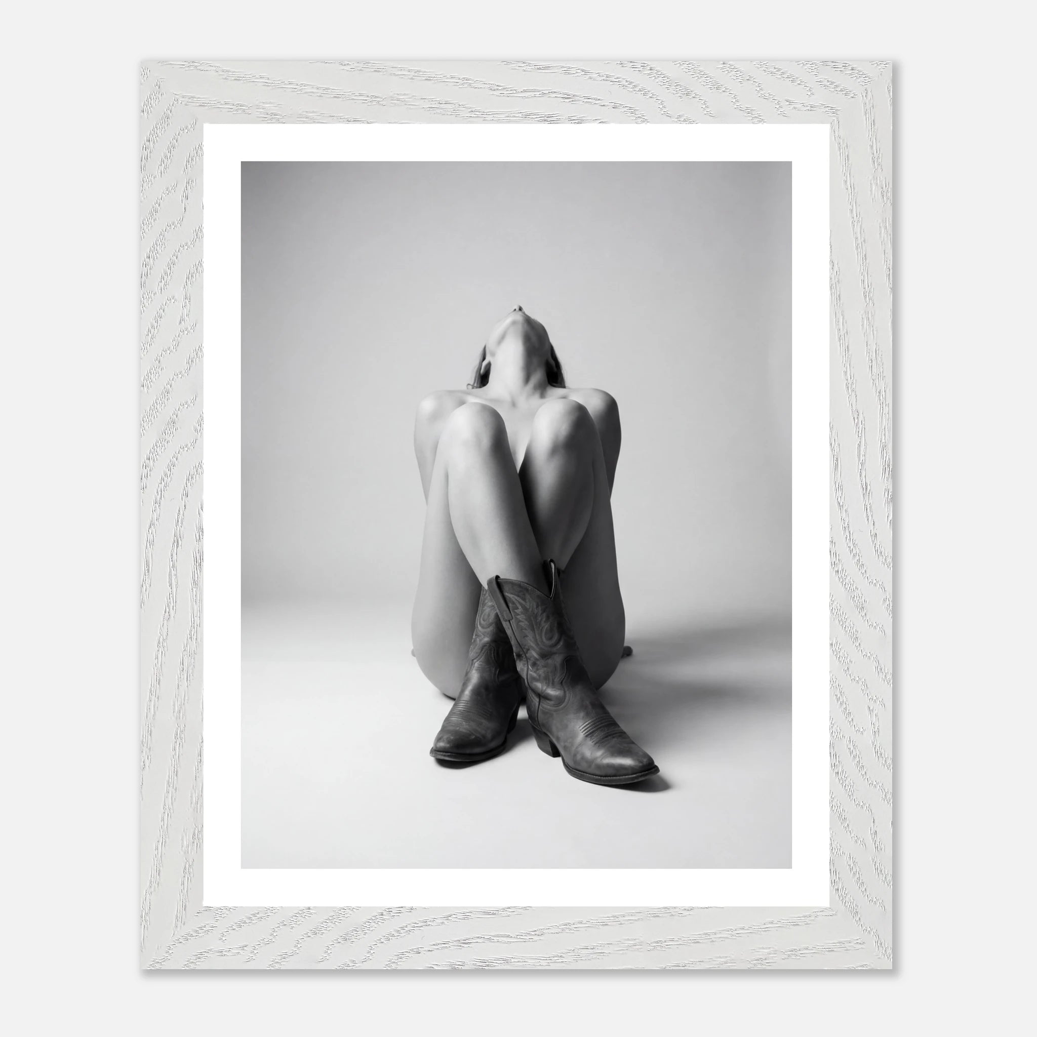 Framed black and white photo of a person wearing cowboy boots sitting on the floor.