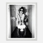 Black and white photograph of a rebellious cowgirl wearing cowboy boots and sunglasses sitting in a tiled restroom holding a cigarette and beer.