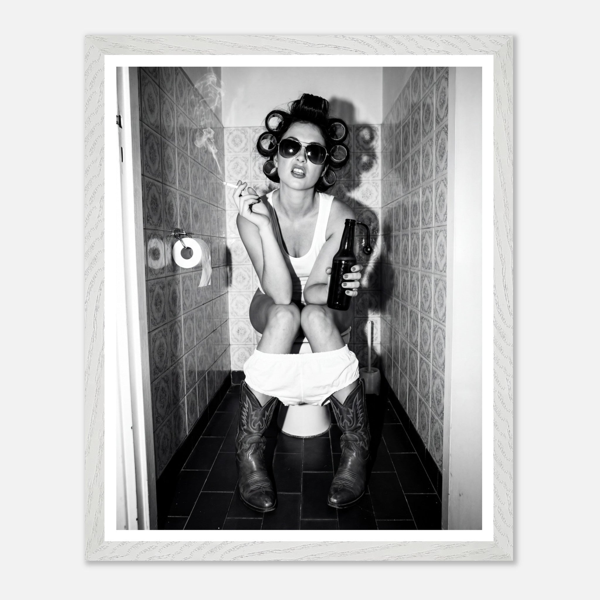 Black and white photograph of a rebellious cowgirl wearing cowboy boots and sunglasses sitting in a tiled restroom holding a cigarette and beer.