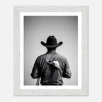 Black and white photograph of a rodeo cowboy viewed from behind wearing a western hat with a numbered rodeo tag pinned to his shirt after competition.